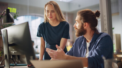 Two Stylish Employees Discussing Work-Related Projects on Computer in Creative Agency in Loft Office. Young Creative Director and Manager Talking About Work, Making Changes on Corporate Project.