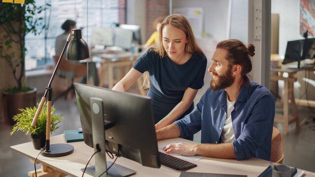 Team of Two Young Entrepreneurs Talking, Discussing Growth Strategy at a Desk with Computers. Stylish Businesspeople Work on an Investment and Marketing Project in a Creative Agency.