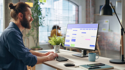 Handsome Long-Haired Bearded Manager Working at a Desk in Creative Office, Using Desktop Computer...