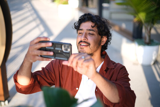 Smiling curly haired man taking a picture using his mobile phone on the sidewalk