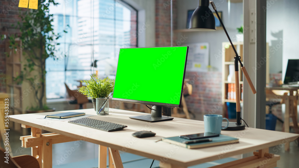 Fototapete Establishing Shot: Desktop Computer Monitor with Green Screen Mock Up Chroma Key Display Standing on a Desk in Modern Creative Office. Cozy Agency Space in Loft Building.