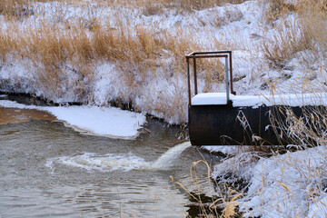 Sewage discharge from pipe into river in winter, river pollution and ecology.