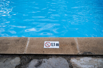 View of a pool and rocks on the floor. Information and precaution sign for the dept of the pool and forbidden to jump off the edge