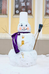 Snowman made of snow with lilac scarf and broom.