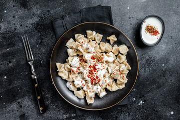 Turkish manti with yoghurt and tomato sauce in a plate. Black background. Top view - obrazy, fototapety, plakaty