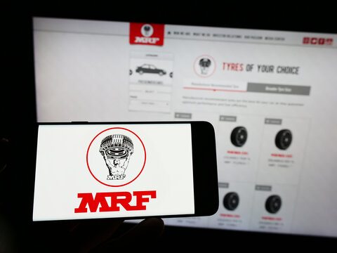Stuttgart, Germany - 12-11-2022: Person holding mobile phone with logo of Indian company Madras Rubber Factory (MRF Tyres) on screen in front of web page. Focus on phone display.