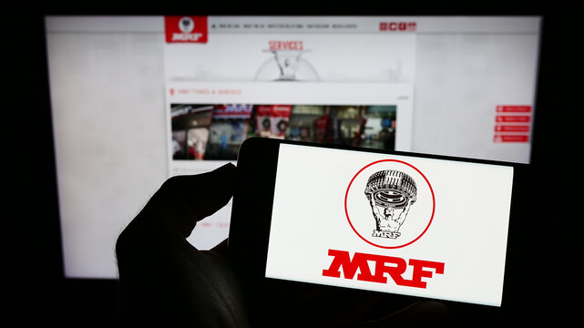 Stuttgart, Germany - 12-11-2022: Person holding cellphone with logo of Indian company Madras Rubber Factory (MRF Tyres) on screen in front of webpage. Focus on phone display.
