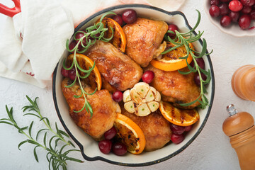 Baked chicken thighs with orange, cranberry and spicy herbs rosemary servered in frying pan on light background. Festive Christmas Dinner Concept menu. Top view. copy space