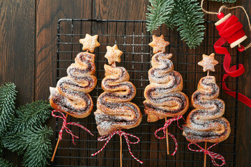 Christmas tree shape puff pastry cakes with chocolate filling, sugar powder and lollipops on old...