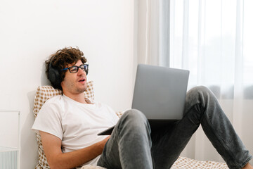 Fototapeta premium Guy using computer notebook, browsing Internet and sitting in bedroom, Young attractive caucasian man sitting on a bed at home working with laptop