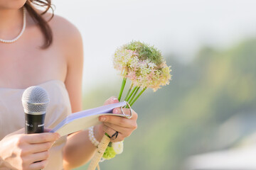 A bouquet of flowers in the hands of a female host, holding a microphone, waiting for the schedule to report the order of the event.