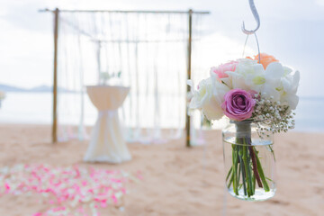 Flowers in glass decorate the wedding arch. There is a set up of the ceremony with roses and orchids arranged on the beach, looking very beautiful.
