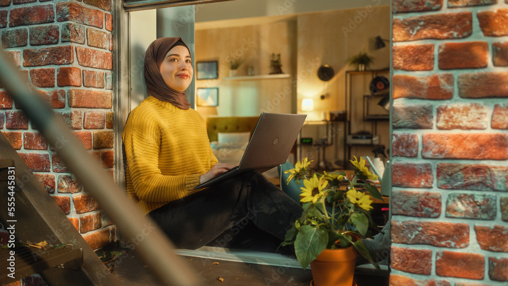 Aufkleber portrait of a young muslim female in hijab working on a laptop computer while sitting on a window si