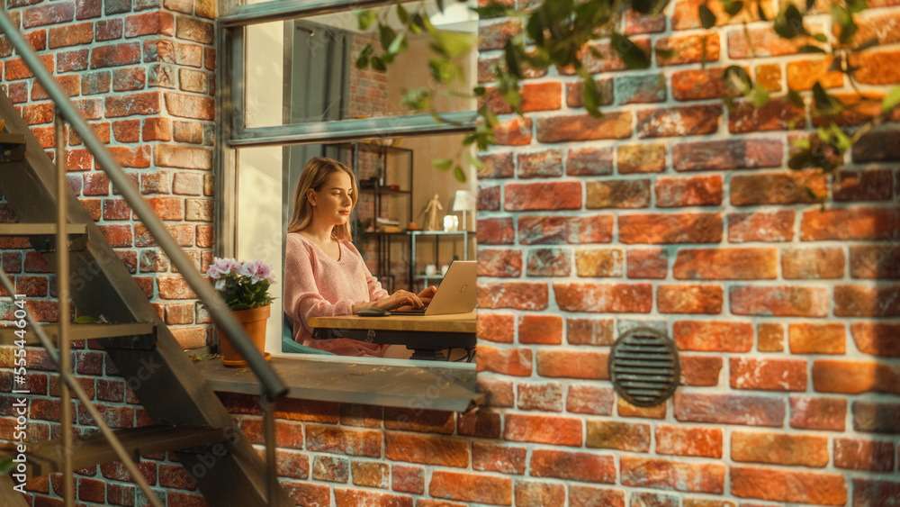 Aufkleber young attractive female in pink sweater working on a laptop computer while sitting behind a table in