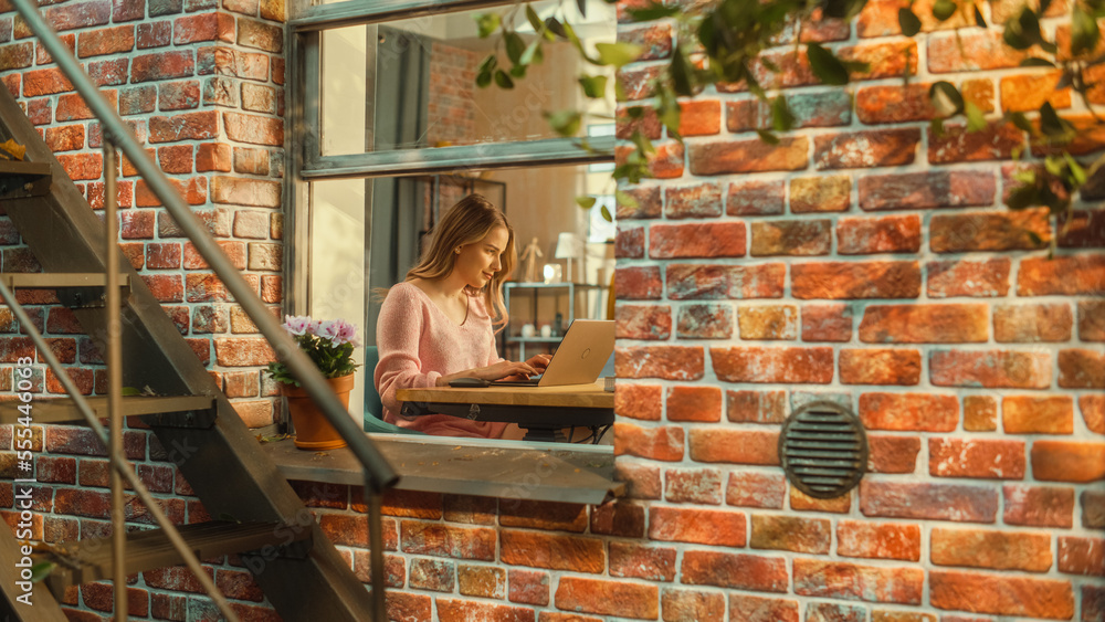 Poster portrait of a young woman working on laptop computer while sitting at home in a multi-storey brick h
