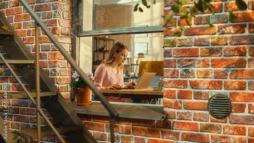 Aufkleber young excited female in pink sweater working on a laptop computer while sitting behind a table in li