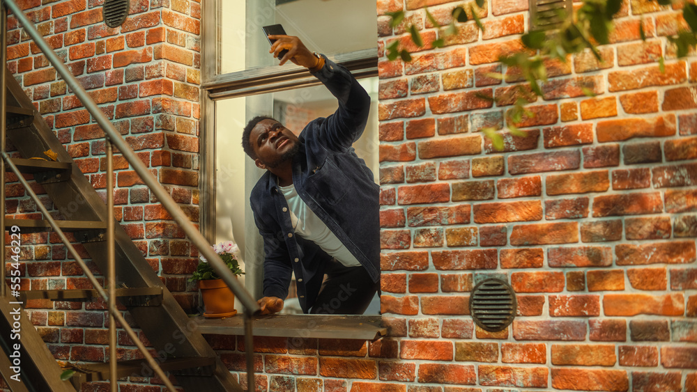 Poster Distressed Young Black Man Doesn't Understand Why There is No Cellular Connection on His Smartphone, Frantically Reaching Out to the Sky with a Mobile Phone from His Apartment Window.