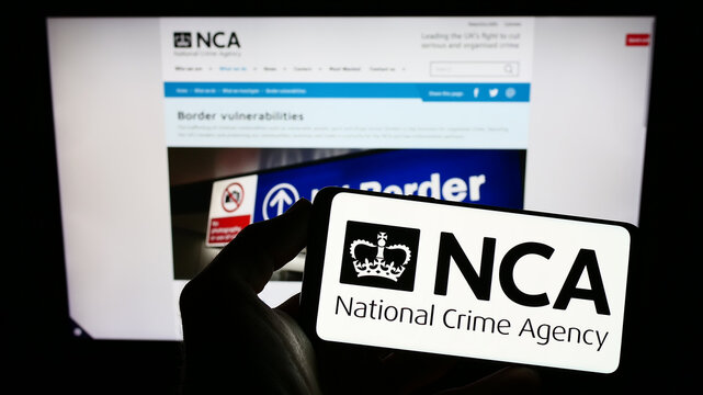 Stuttgart, Germany - 12-14-2022: Person holding mobile phone with logo of British National Crime Agency (NCA) on screen in front of web page. Focus on phone display.
