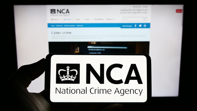 Stuttgart, Germany - 12-14-2022: Person holding cellphone with logo of British National Crime Agency (NCA) on screen in front of webpage. Focus on phone display.