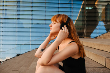 Ginger young woman listening to music with headphones outdoors