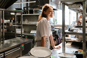 Fototapeta na wymiar Beautiful woman chef cook smiling while standing in kitchen of a restaurant