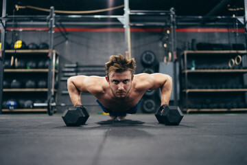 Obraz na płótnie Canvas Strong man doing push-ups using dumbbells
