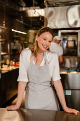 Cheerful woman chef cook standing in kitchen of a restaurant