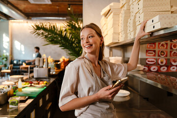 Smiling young woman preparing takeaway food in restaurant - 555453640