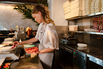 Beautiful woman chef cook weighing tomatoes on scales while preparing meals for a restaurant in kitchen