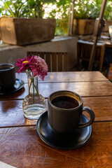 cup of coffee wooden table in the background vase with purple flowers in the background vegetation