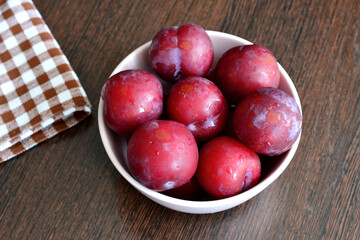 purple garden plums in the bowl on wooden kitchen table with napkin, macro