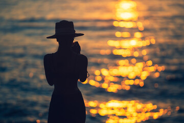 Silhouette woman standing in ocean sea during summer sunset on blurred background.