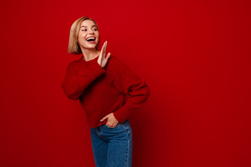 Excited woman waving hand and looking aside isolated over red background