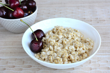 boiled oatmeal in the bowl with garden cherries isolated, macro