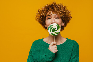Curly ginger woman smiling while posing with lollipop