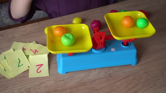 little girl plays in the store, weighs vegetables on a toy scale, and studies the numbers, close-up, the concept of children's home learning games