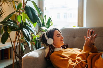 Young white woman in headphones using cellphone while lying on couch