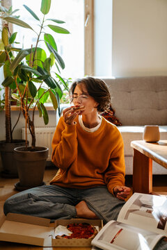 Young white woman in eyeglasses eating coffee while sitting on floor