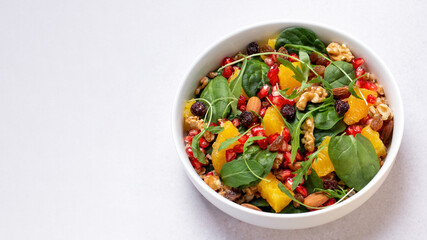 Healthy salad with spelt, oranges, pomegranate seeds. greens and nuts on light background, minimal style