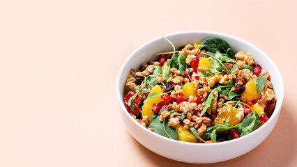 Healthy salad with spelt, oranges, pomegranate seeds. greens and nuts on light background, minimal...