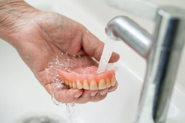 Asian senior or elderly old woman patient holding and washing denture in nursing hospital ward;...