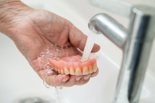 Asian senior or elderly old woman patient holding and washing denture in nursing hospital ward; healthy strong medical concept