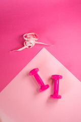 Pink dumbbells lie on a yoga mat tape of measuring waist size Pink background.Slimming, yoga, sports,healthy diet