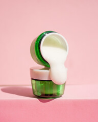 Skin cream flows from a green jar. Cosmetics pink background .Geen jars with a cosmetic product Close up 1