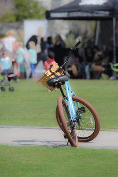 A powder blue bicycle with a straw basket stands alone during an outdoor festival