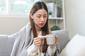 Sick, influenza asian young woman, girl headache have fever, hand touching forehead, holding thermometer for check measure body temperature, illness while sitting rest on sofa at home. Health care.