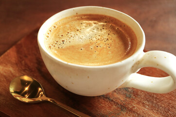 Closeup of a hot frothy coffee with brass teaspoon on wooden table