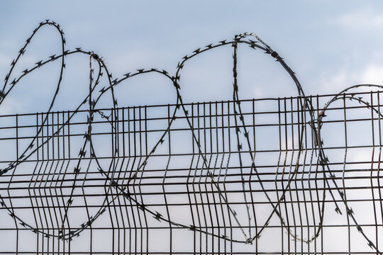 Metal fence with curved barbed wire along the top; England