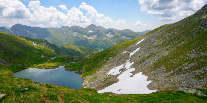 high altitude mountain lake. beautiful nature landscape of romania. grass and snow on the hills. sunny weather with clouds on the sky in summer