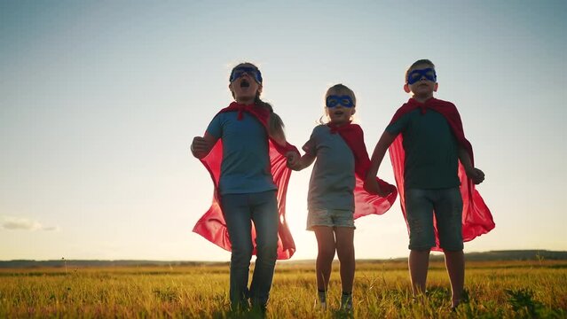 team superhero. a group of children are running across the field in a superhero dream costume with a silhouette of a sunset red cape. the concept of a happy family childhood. teamwork superhero